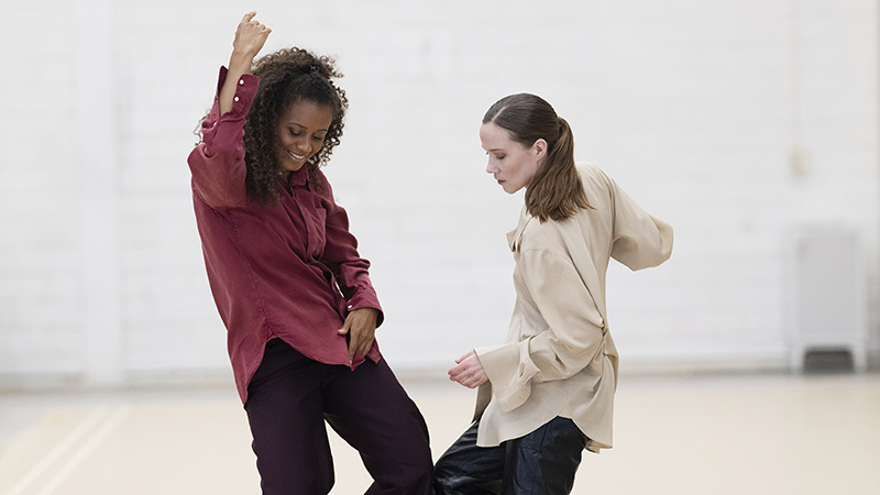 Två dansare i en stor ljus sal, fångade i rörelse)
