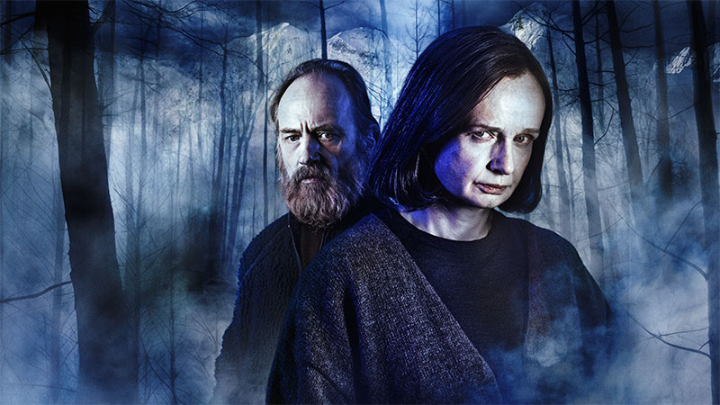 Två av skådespelarna mot en bakgrund av suggestivt dimmig skog.)