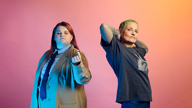 De två medverkande skådespelarna poserar mot en bakgrund i skärt och rosa.)