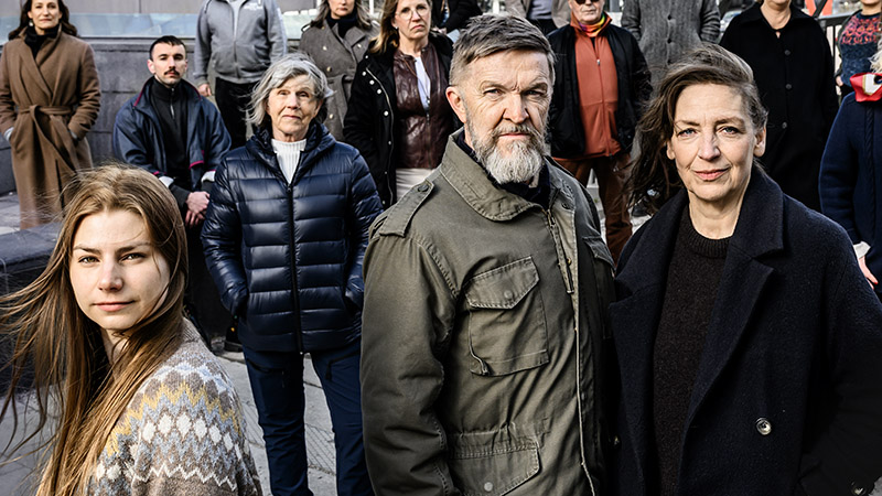 Bild i stadsmiljö. I förgrunden tre av de medverkande (Klara Pasma, Timo Nieminen, Margareta Stone), i bakgrunden statister som också tittar mot kameran.)