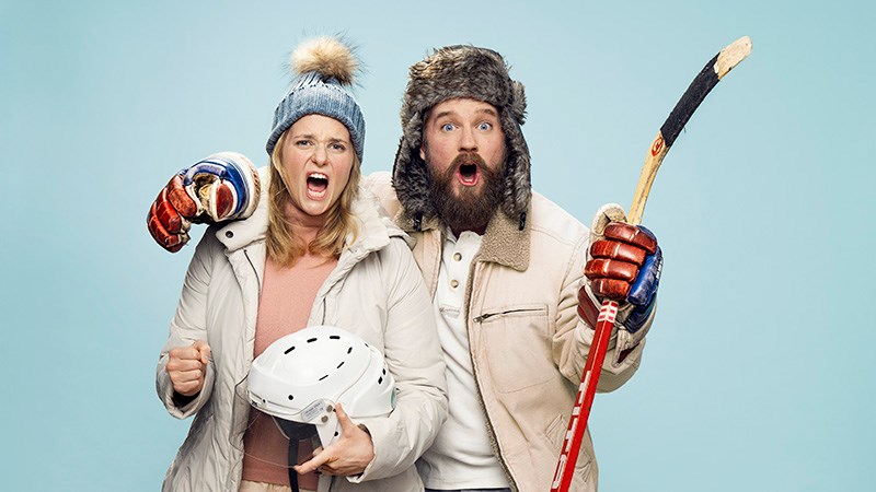 Två personer klädda i vinterkläder som ser ut att heja på en match. Till vänster Stina Nordberg hållandes en hockeyhjälm, till höger Philip Lithner hållandes en hockeyklubba.)