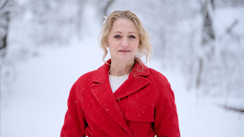 Maria Sundbom i röd rock mot en bakgrund av ett snöbeklätt vinterlandskap.)
