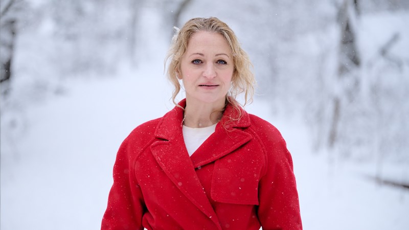 Maria Sundbom i röd rock mot en bakgrund av ett snöbeklätt vinterlandskap.)