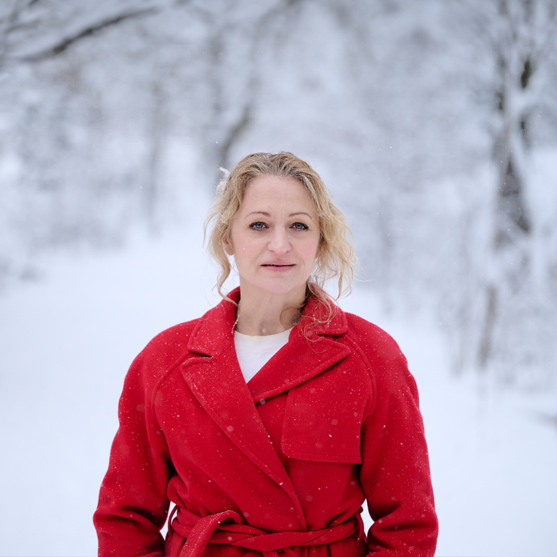 Maria Sundbom i röd rock mot en bakgrund av ett snöbeklätt vinterlandskap.