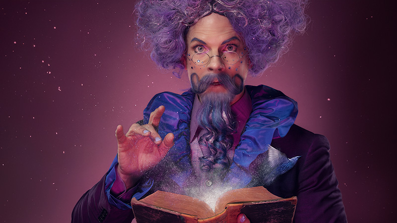 Skådespelare utklädd till Herr Klex, med lila lockigt hår och långt skägg.)